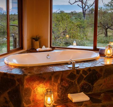 Luxurious bathtub with lanterns and a view of the wilderness at Arathusa Safari Lodge.