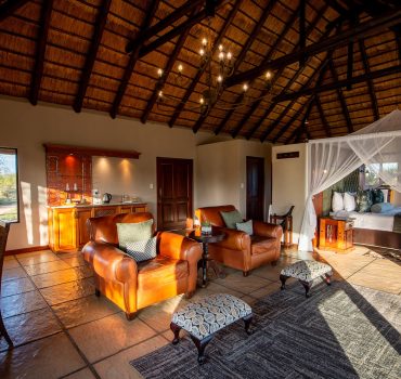 Spacious and luxurious water-facing suite with living area and canopy bed at Arathusa Safari Lodge.