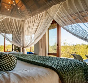 Elegant canopy bed with views of the surrounding wilderness at Arathusa Safari Lodge.