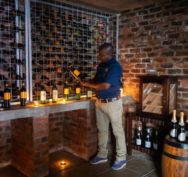 Wine cellar at Arathusa Safari Lodge showcasing a variety of wines with a staff member examining a bottle.