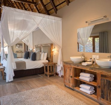 Spacious and elegant water-facing suite with canopy bed and double sinks at Arathusa Safari Lodge.