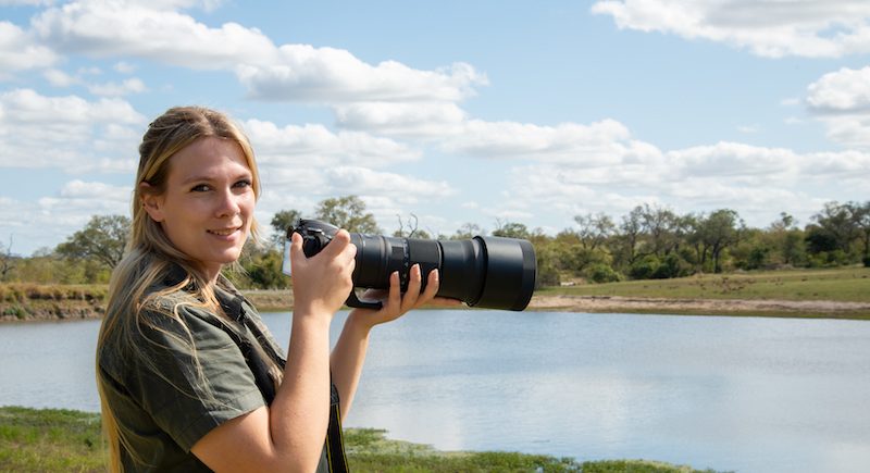 blonde-lady-holding-a-camera-outside-by-a-waterhole