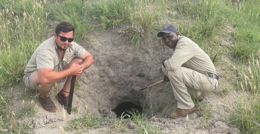 two-men-crouching-next-to-a-termite-mound-hole